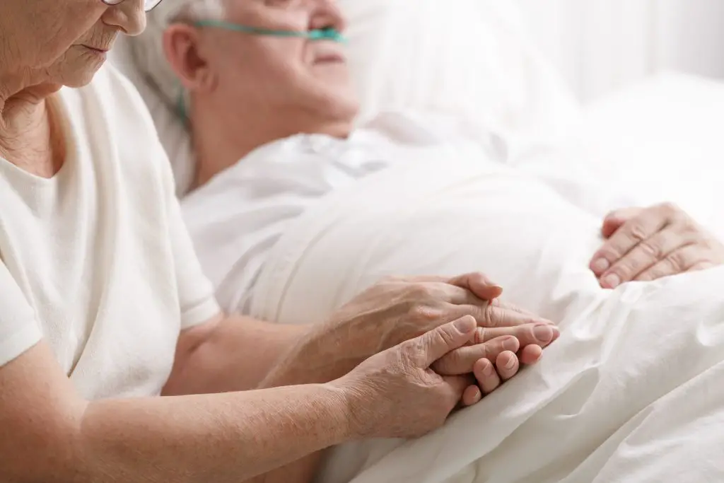 Senior married couple holding hands in hospital.