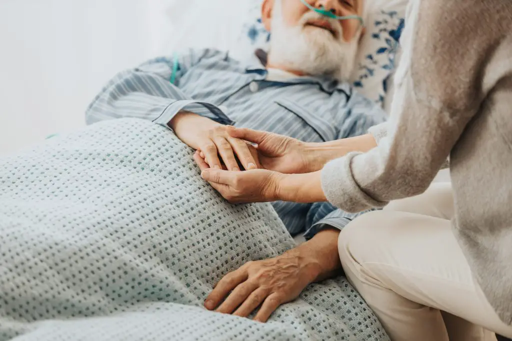 Close-up of older dying man holding his wife's hands.